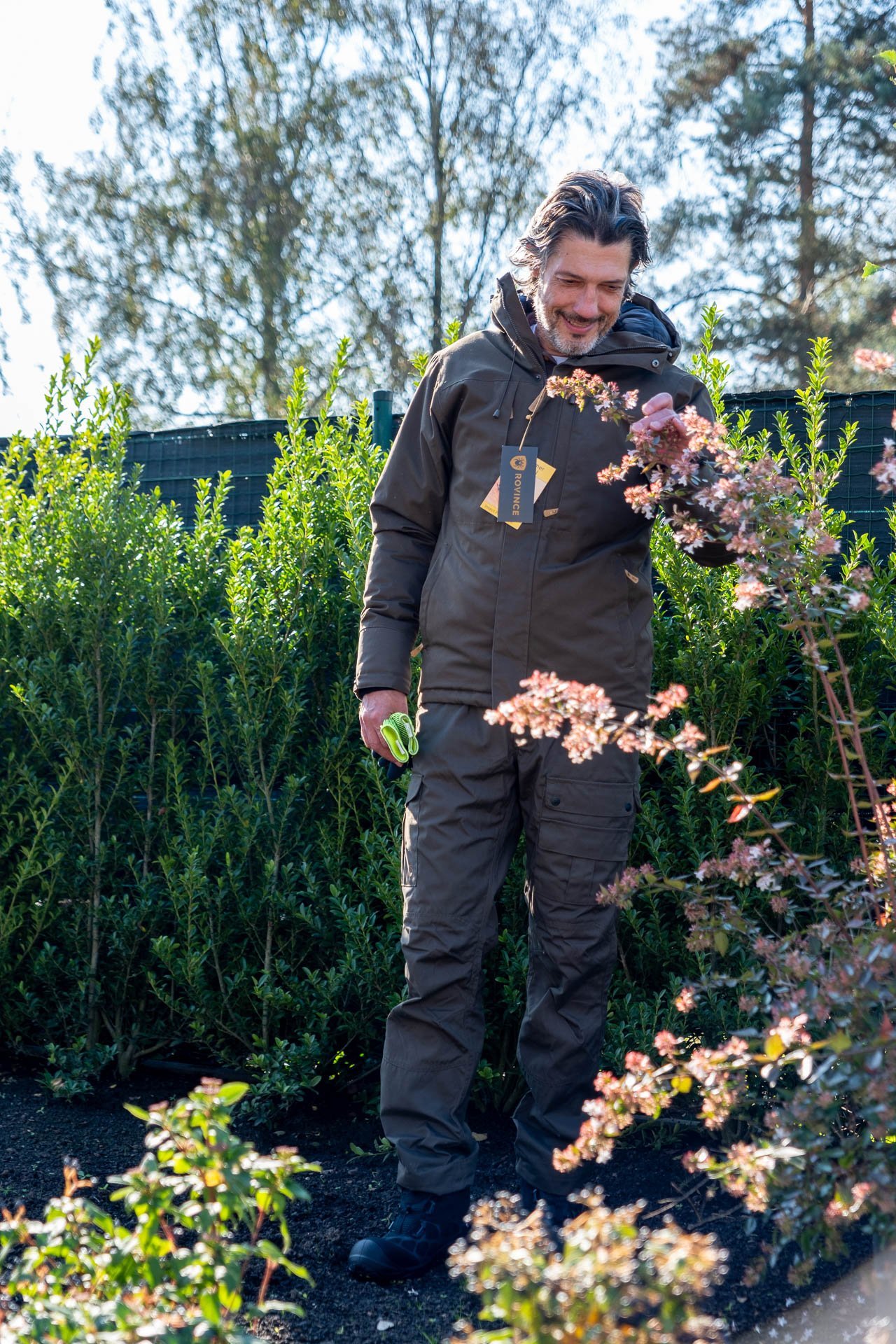 Man in tuin geniet van de natuur, gekleed in bedrijfskleding. Samenwerking met Limburgs Landschap: Bedrijfskleding met een Verhaal.
